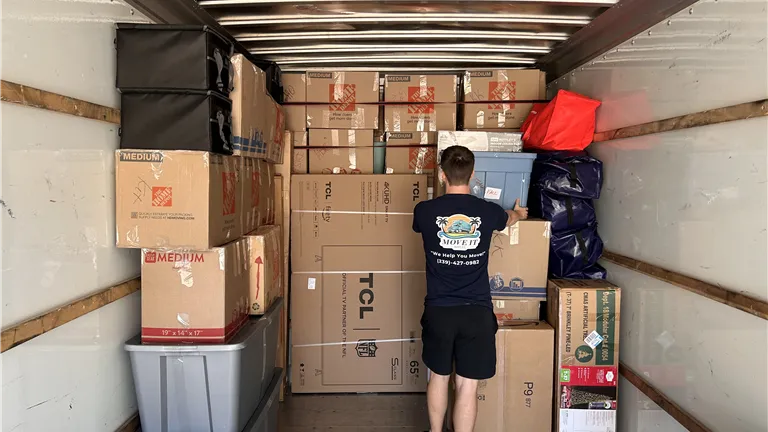 Two men loading cardboard boxes onto a truck in a warehouse.