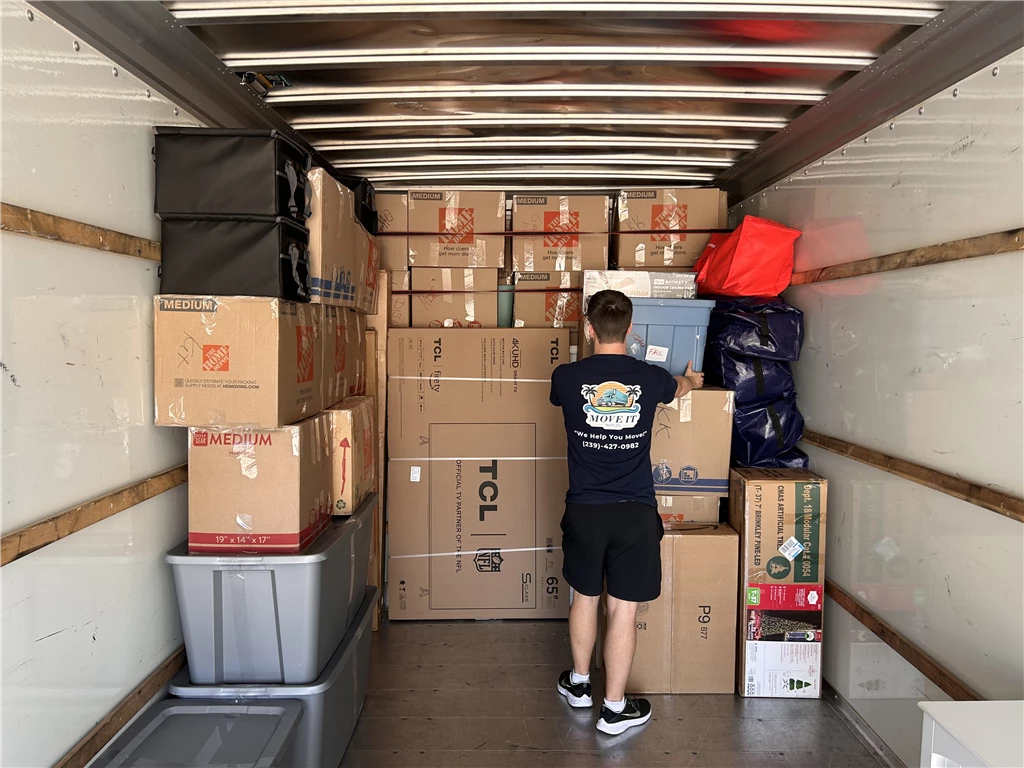 Two men loading cardboard boxes onto a truck in a warehouse.