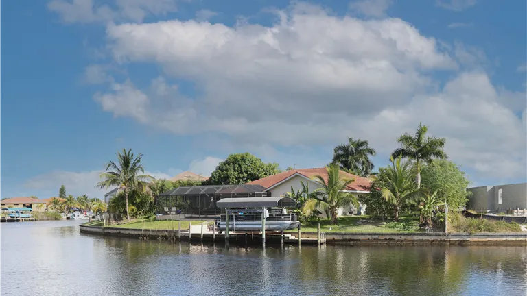 Scenic view of a tropical waterfront home in Cape Coral, Florida with palm trees and blue sky.