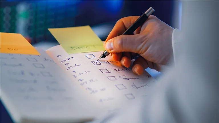 Close-up of a hand writing in a notebook with checkboxes, highlighting productivity and organization.