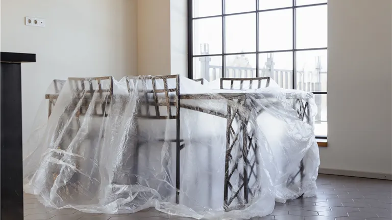Dining chairs and table covered in plastic, a new home interior ready for moving in.
