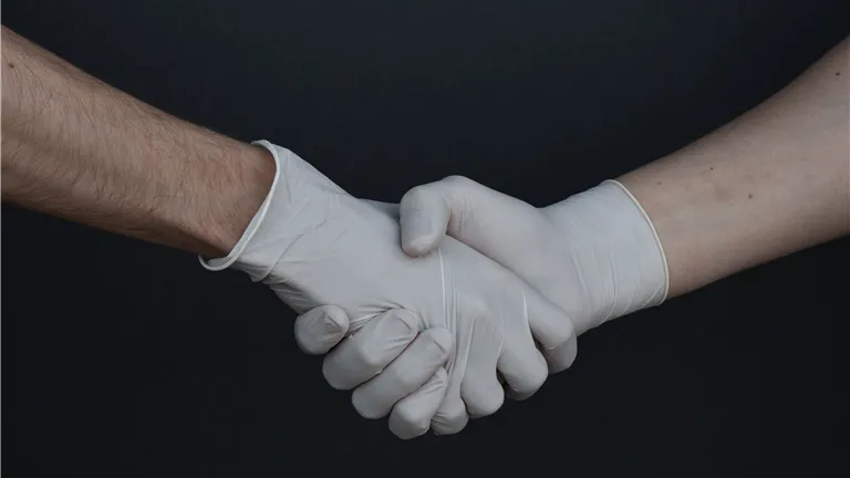 Two people shaking hands while wearing latex gloves, illustrating safety and protection.