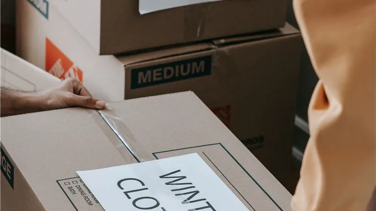 Close-up of people packing labeled boxes for moving day at home.