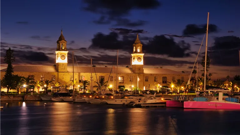 A stunning nighttime view of the Royal Navy Shipyard in Bermuda with illuminated clock towers and yachts.