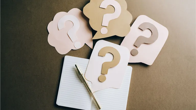 Flat lay of question mark paper crafts on a notebook, symbolizing questions and ideas.