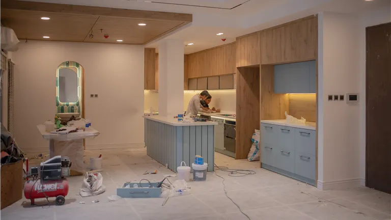 A modern kitchen undergoing renovation, featuring a worker, tools, and materials.