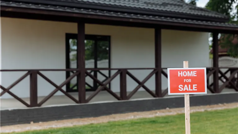 White house with porch and 'Home for Sale' sign on a sunny day.